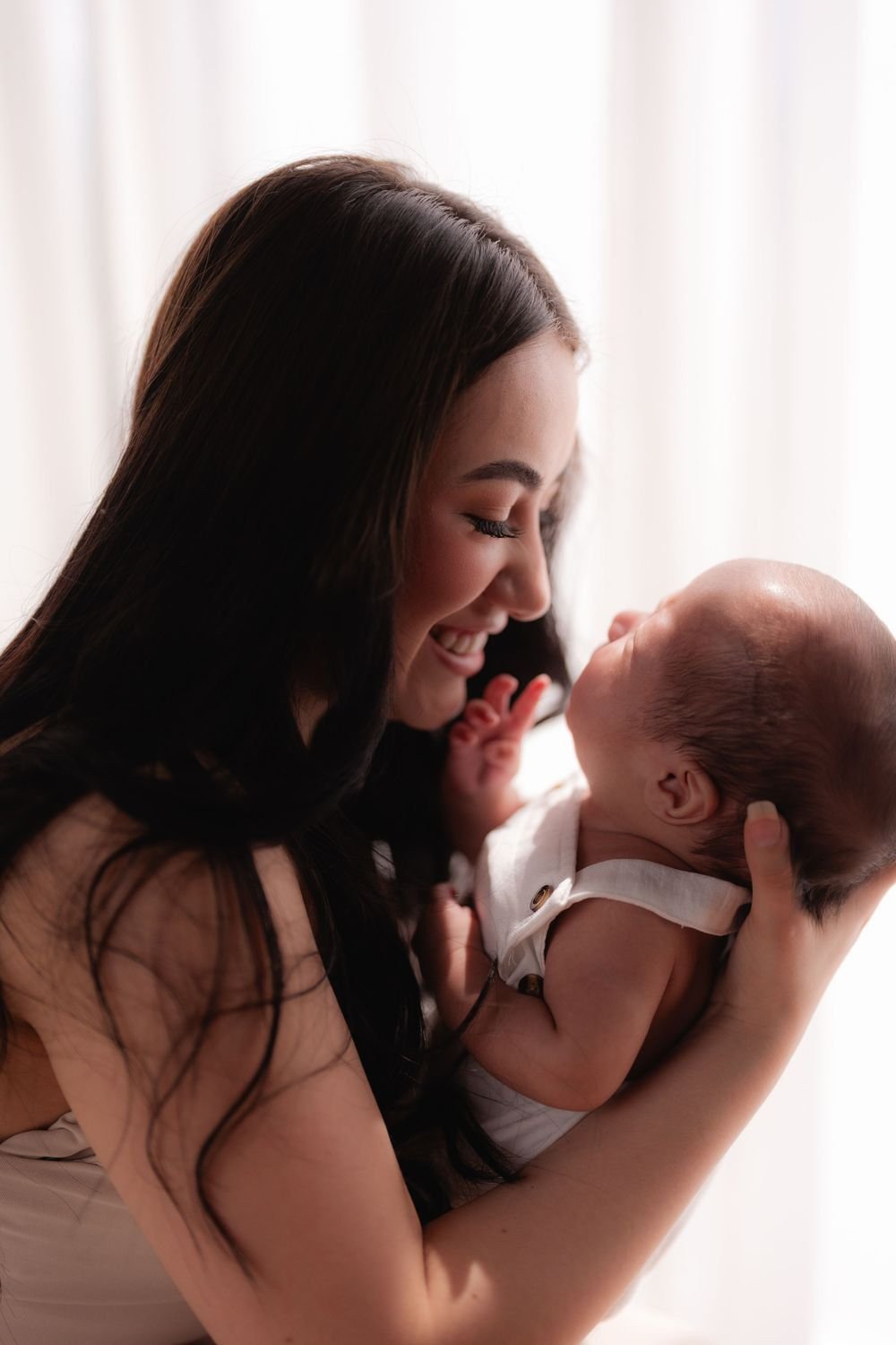 Una mamá sonríe y acerca la cara a la de su bebé recién nacido.