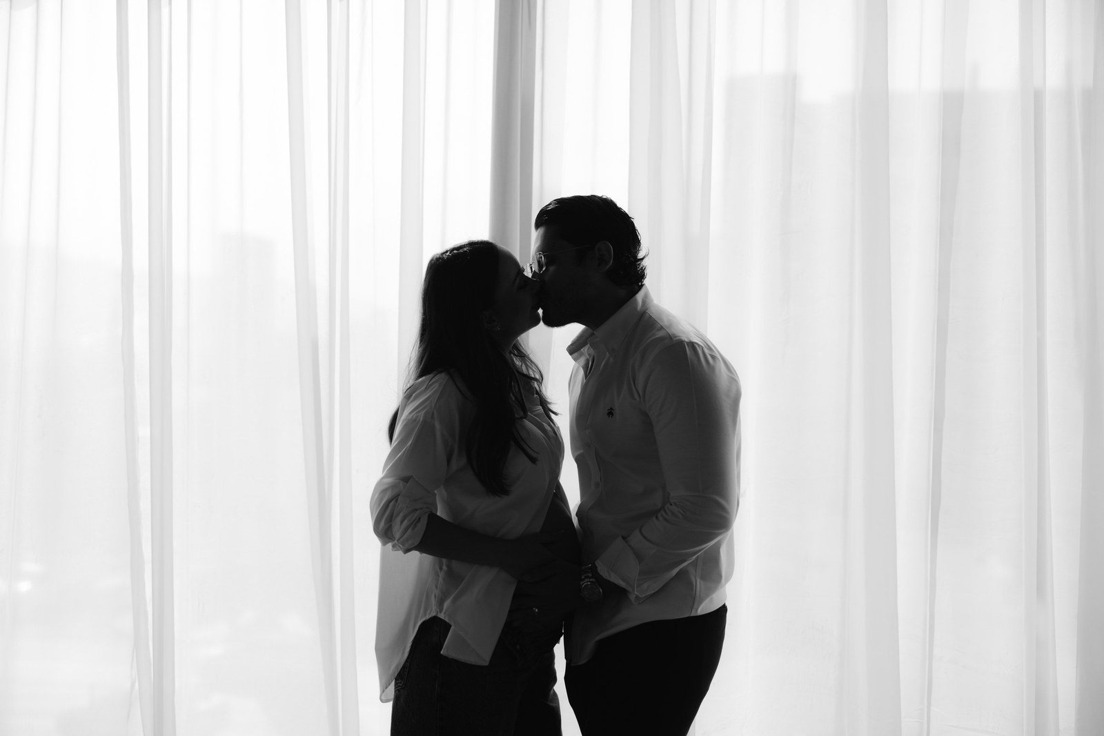 Silueta de una pareja que se besa frente a unas cortinas blancas.