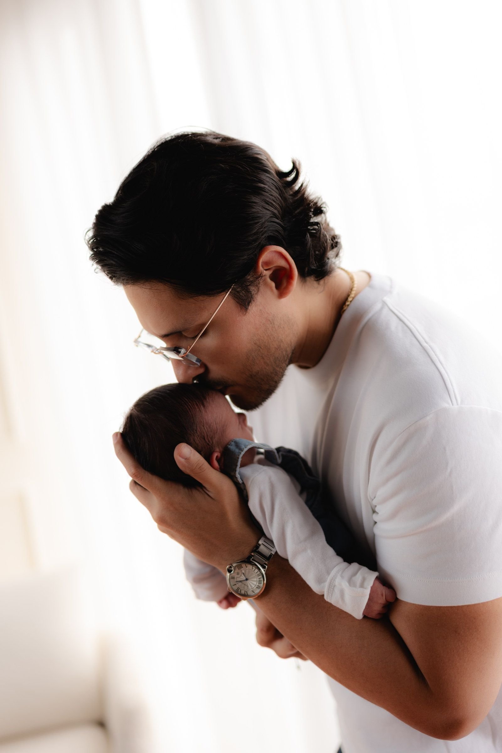 Un papá besa la cabeza de su bebé recién nacido, con la cara inclinada hacia él.