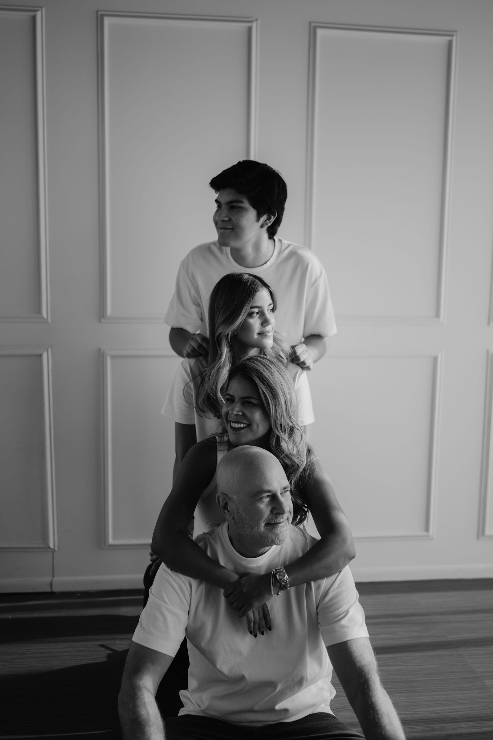 En blanco y negro, una familia se apila en broma uno sobre otro frente a una pared con molduras.