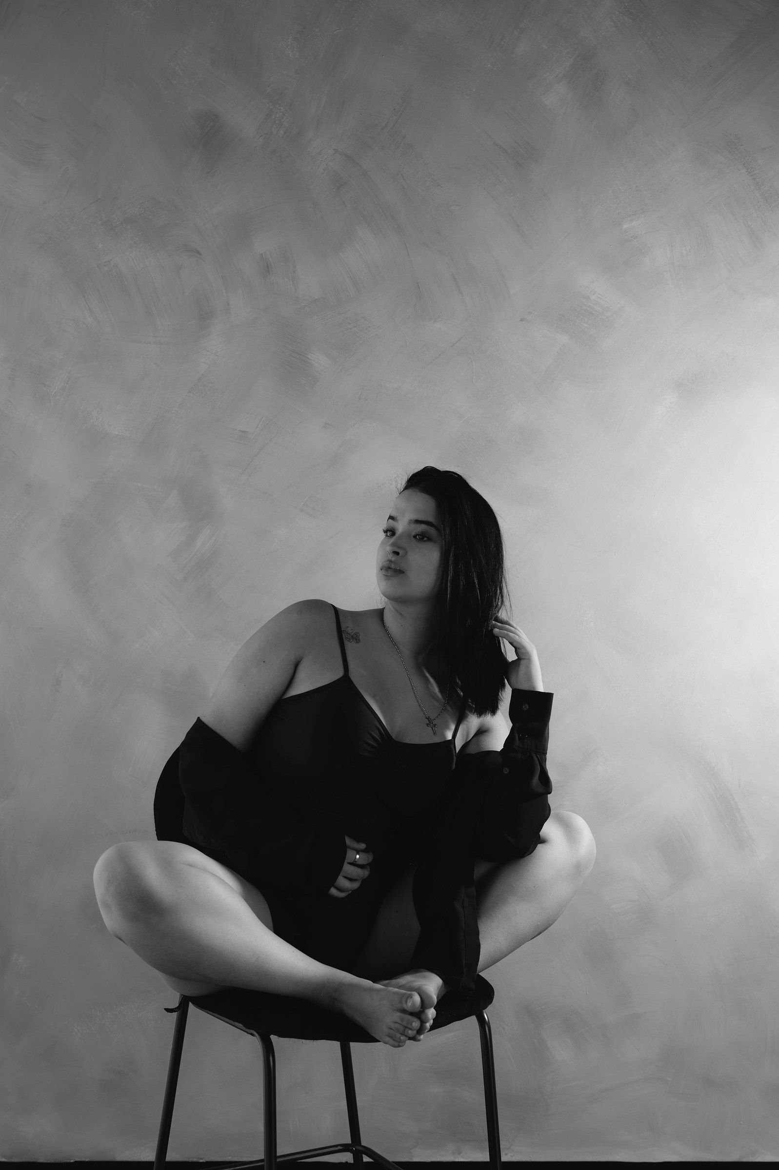 En blanco y negro, una mujer se sienta en un banco con las piernas cruzadas y mira hacia un lado.