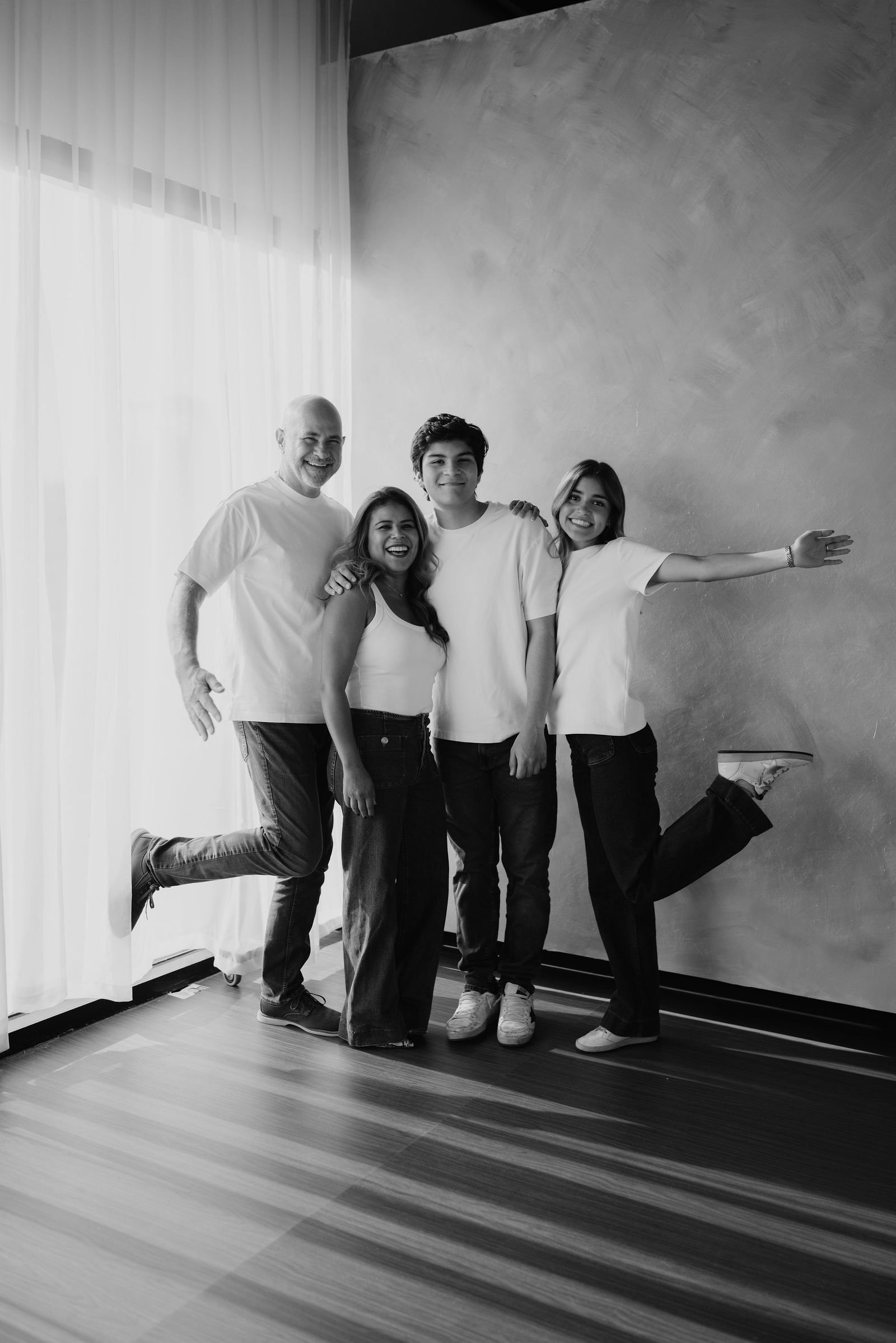 En blanco y negro, una familia posa en el estudio con gestos espontáneos y los brazos abiertos.