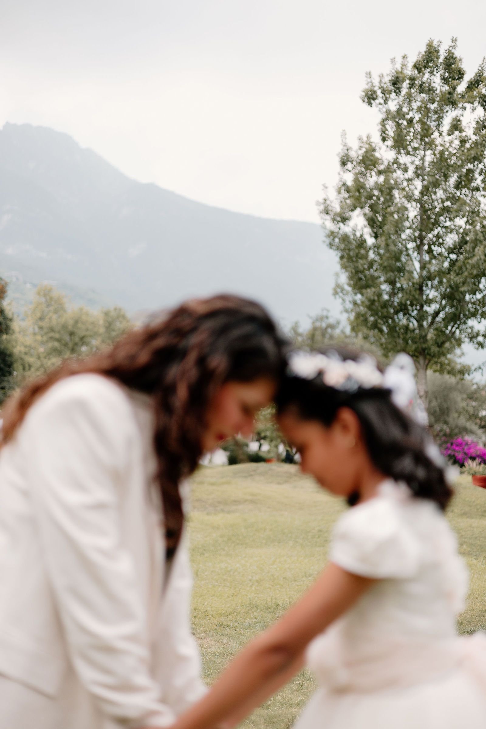 Una mamá y su hija se miran frente a frente al aire libre, con montañas al fondo.