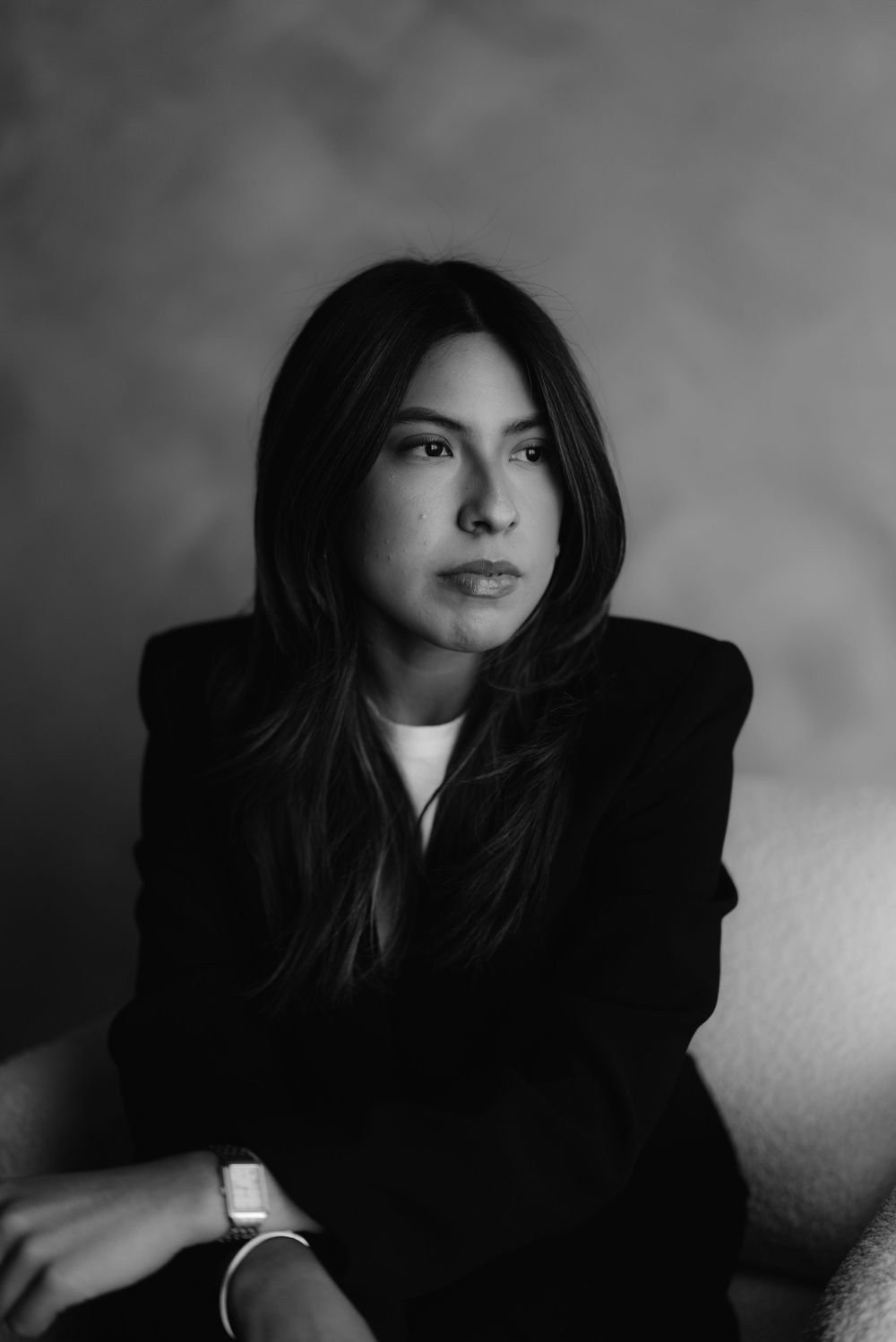 En blanco y negro, una mujer de cabello largo y saco oscuro mira a la cámara.