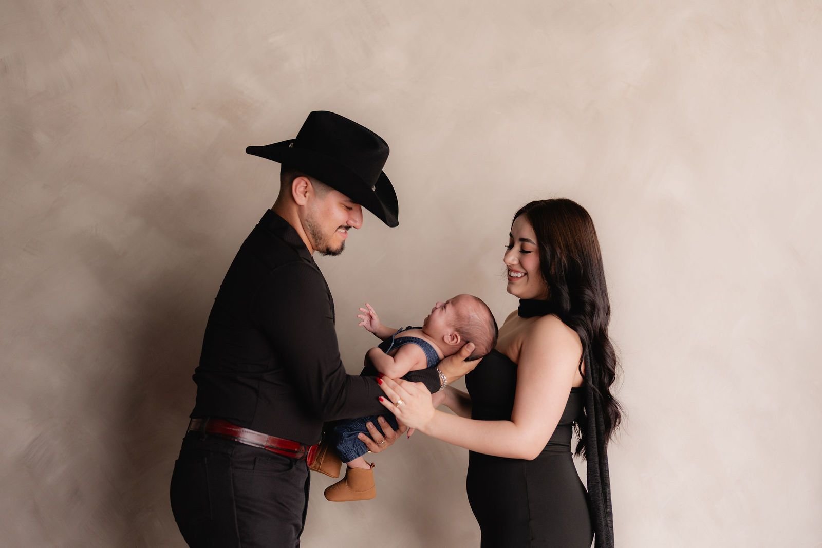 Un papá con sombrero vaquero sostiene a su bebé recién nacido junto a la mamá.